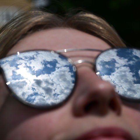 Der Himmel mit lockeren Wolken spiegelt sich in der Sonnenbrille einer Frau