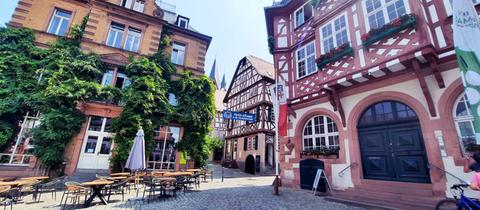 Foto von Altstadtgassen mit Fachwerkhäusern, begrünten Gebäuden, Tischen und Stühlen einer Gastronomie.
