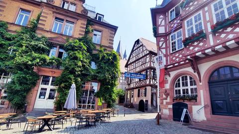 Foto von Altstadtgassen mit Fachwerkhäusern, begrünten Gebäuden, Tischen und Stühlen einer Gastronomie.