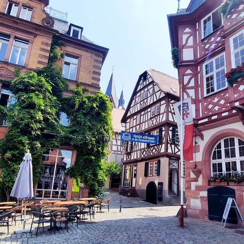 Foto von Altstadtgassen mit Fachwerkhäusern, begrünten Gebäuden, Tischen und Stühlen einer Gastronomie.