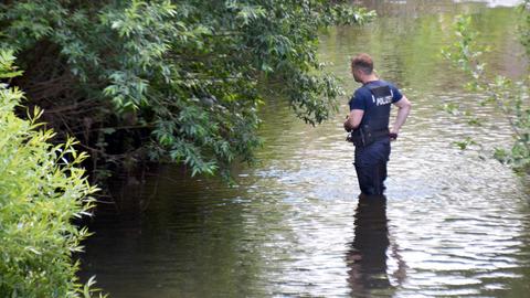 Ein Polizist steht kniehoch in einer Wasserfläche, umgeben von Gebüsch.