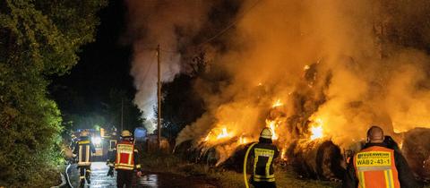 Auf einer Wiese löschen Feuerwehrleute einen Haufen brennender Heuballen.