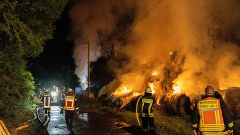 Auf einer Wiese löschen Feuerwehrleute einen Haufen brennender Heuballen.