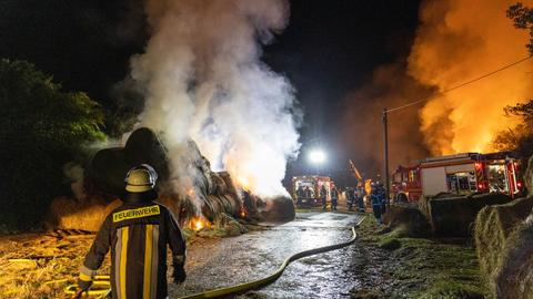 Auf einer Wiese löschen Feuerwehrleute einen Haufen brennender Heuballen.