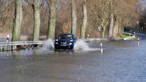 Ein Autofahrer fährt über eine überflutete Landstraße bei Heuchelheim.