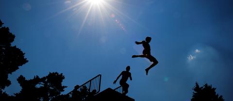 Zwei Kinder springen von einem Sprungturm im Schwimmbad