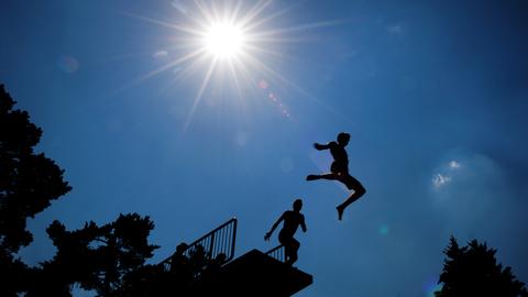 Zwei Kinder springen von einem Sprungturm im Schwimmbad