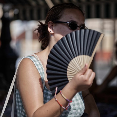 Frau mit Sonnenbrille wedelt sich mit Fächer Luft zu.