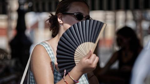 Frau mit Sonnenbrille wedelt sich mit Fächer Luft zu.