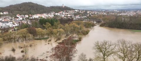 Luftaufnahme einer überfluteten Wiesenlandschaft, im Hintergrund liegt die Stadt Fulda. 