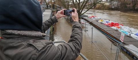 Ein Passant fotografiert einen Fluss, der über die Ufer getreten ist.