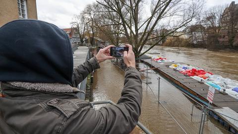 Ein Passant fotografiert einen Fluss, der über die Ufer getreten ist.