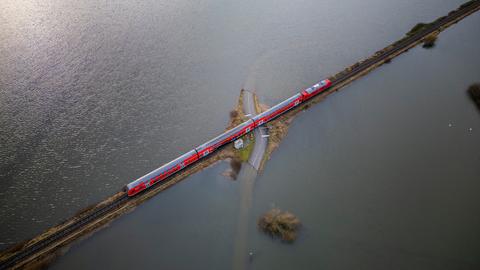 Luftaufnahme einer Regionalbahn, die über einen Schienendamm durch ein überflutetes Gebiet fährt.