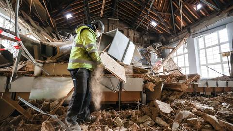 Ein Arbeiter in Schutzkleidung räumt Schutt in einem Saal auf.