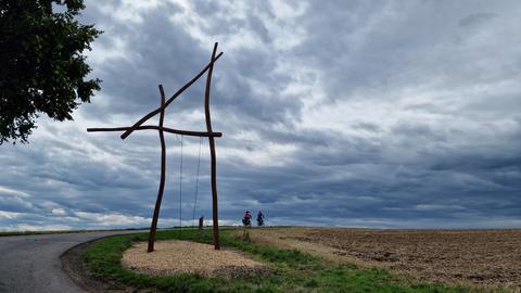 Radfahrer vor Himmel mit dunklen Wolken, im Vordergrund Riesen-Schaukel