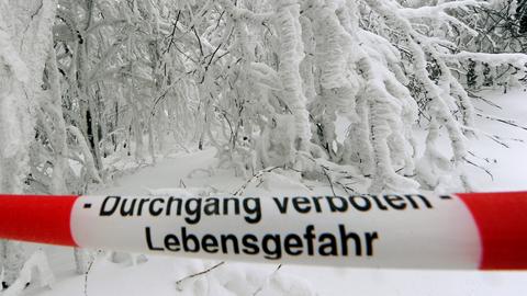 "Durchgang verboten - Lebensgefahr" steht auf einem rot-weißen Absperrband vor einer schneebedeckten Straße.