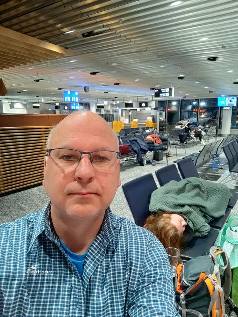 Ein Selfie - daneben liegt eine Frau auf Bänken im Flughafen und schläft.