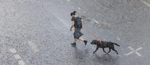 Eine Frau rennt mit ihrem Hund bei Starkregen über eine überflutete Straße.