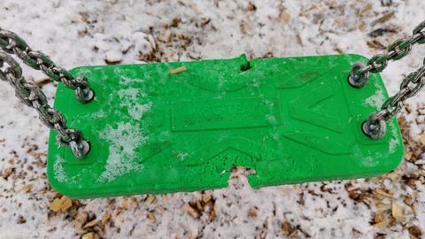 Das Bild zeigt eine grüne Schaukel mit Bissspuren auf einem Spielplatz 
