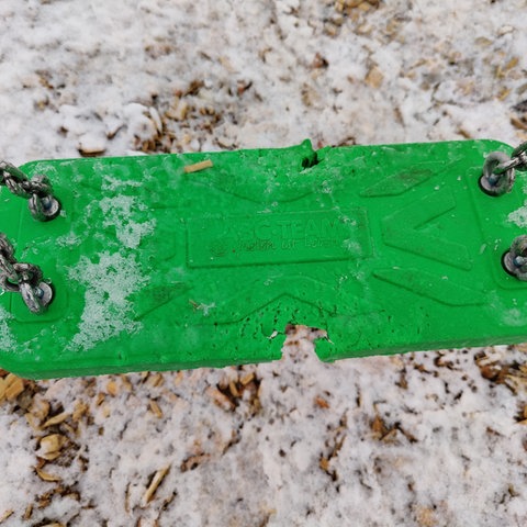 Das Bild zeigt eine grüne Schaukel mit Bissspuren auf einem Spielplatz 