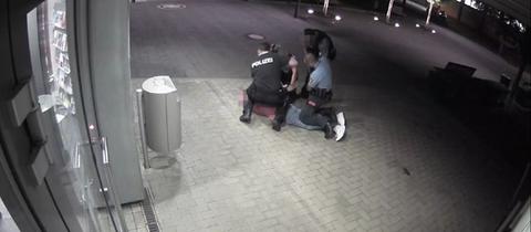Überwachungsvideo aus Idstein zeigt mutmaßliche Polizeigewalt: Drei Menschen in Polizeiuniformen knien auf einer Person, die auf dem Boden liegt. Ein Vierter steht daneben.