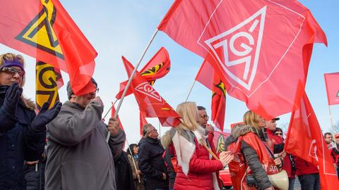 Beschäftigte schwenken bei einem Warnstreik IG-Metall-Fahnen 