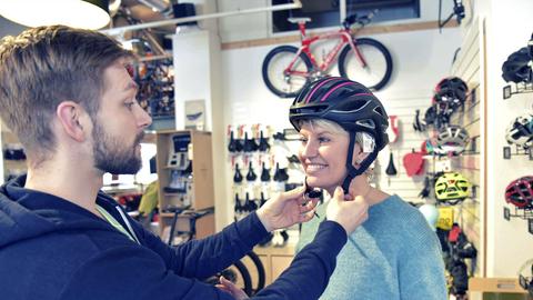 Ein Verkäufer hilft einer Kundin beim Anprobieren eines Fahrradhelms.