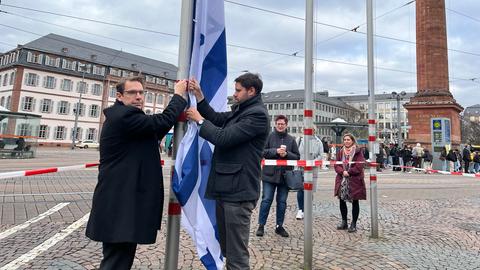 Zwei Männer stehen vor einem Fahnenmast und ziehen eine israelische Flagge hoch.