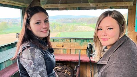 Zwei junge Frauen sitzen in einem Hochsitz und schauen in die Kamera.