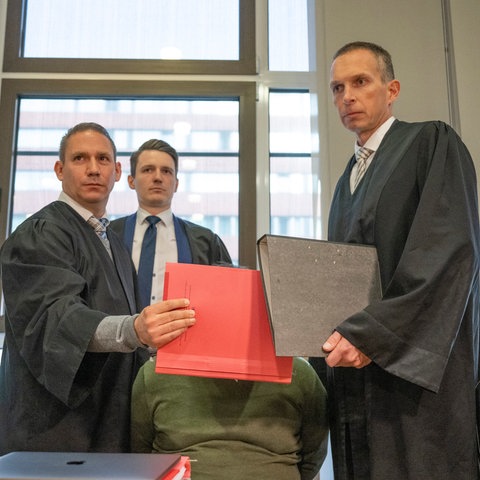 Mit Aktenmappen schirmen die Anwälte den Angeklagten im Verhandlungssaal des Landgerichts in Frankfurt vor den Blicken der Kameras ab. 