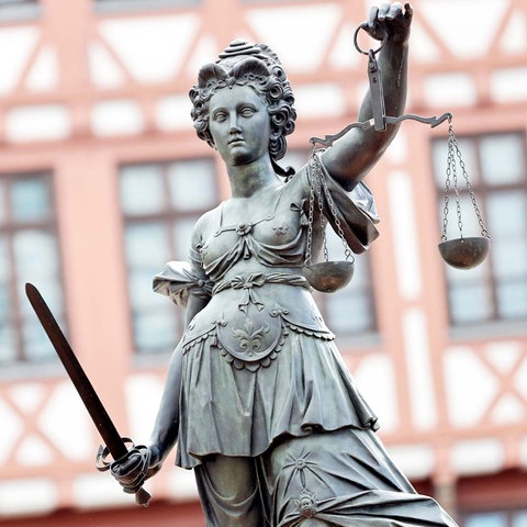 Statue der Justizia vor einer historischen Fachwerkhausfassade.