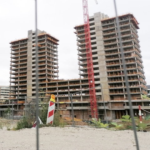 Drei Hochhäuser im Rohbau, umgeben von Kran und Baustellenzaun.