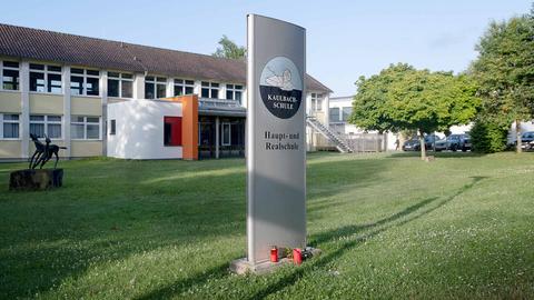 Ein Schulgebäude in der Außenansicht. Davor eine Stele mit dem Logo und Schriftzug "Kaulbach-Schule - Haupt- und Realschule". Am Fuß der Stele stehen Grablichter.