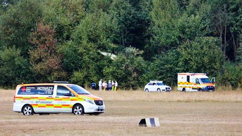 Rettungsfahrzeuge stehen auf einem Flugplatz, im Hintergrund hängt ein abgestürztes Segelflugzeug in einer Baumkrone.