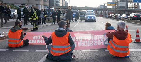 Demonstrierende der Gruppe "Letzte Generation" sitzen auf der Straße und halten Banner hoch.