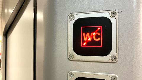 Foto einer Leuchtanzeige, mit einer durchgestrichenen, roten "WC"-Aufschrift. Im Hintergrund unscharf Blick in einen Zug.