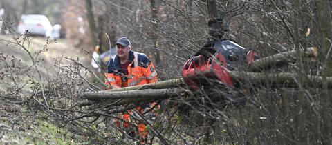Ein Mitarbeiter der Straßenmeisterei räumt mit Hilfe eines Baggers an einer Straße einen abgebrochenen Baum weg.