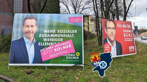 Zwei Wahlplakaten nebeneinander auf einer Rasenfläche am Straßenrand: Michael Kolmer von den Grünen und Hanno Benz von der SPD.
