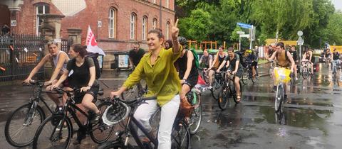 Viele Fahrradfahrenden auf einer Straße, die teils in die Kamera winken.