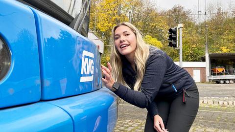 Eine Frau beugt sich zur Vorderseite einer Straßenbahn und streichelt die blau lackierte Oberfläche mit der Signatur "KVG".