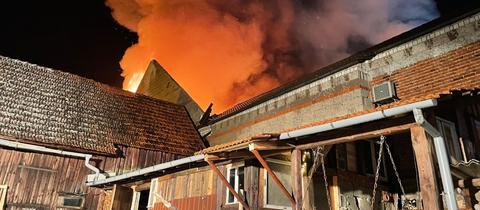 Flammen schlagen aus dem Dach einer Lagerhalle im Dunkeln.