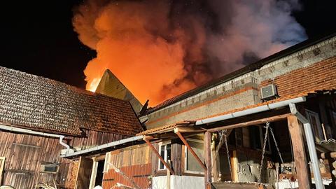 Flammen schlagen aus dem Dach einer Lagerhalle im Dunkeln.