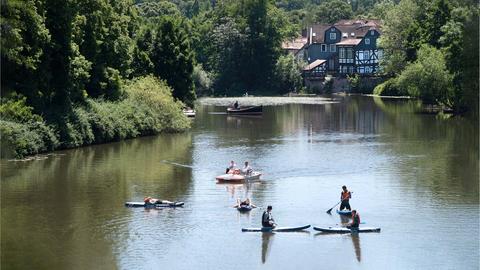 Menschen auf Stand-Up-Paddleing-Boards und in kleinen Booten auf der Lahn. Am grünen Ufer ein Fachwerkhaus.