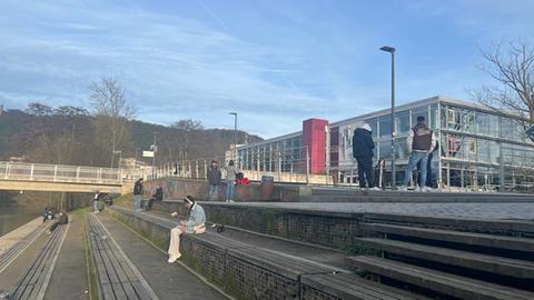 Menschen sitzen und stehen auf Stufen vor Unigebäude