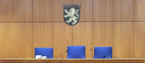 Im Gerichtssaal des Land- und Amtsgerichtes Frankfurt. Drei leere Richterstühle in Detailaufnahme, darüber hängt das hessische Wappen.