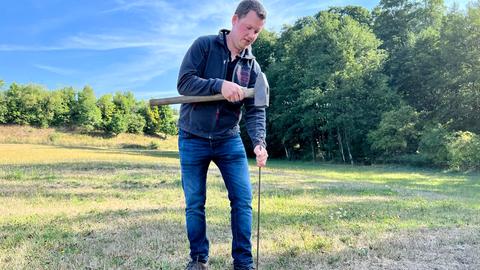 Landwirt Julian Rühl treibt eine Metallstange auf einer Wiese im Jägertal in den Boden mit seinen historischen Überresten eines Jagdlagers. 
