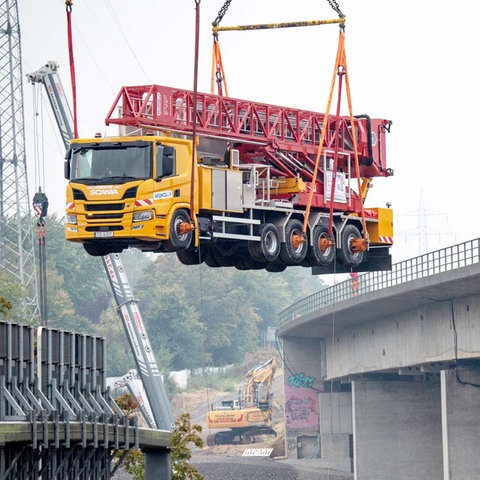 Ein Kran hebt einen Lastwagen durch die Luft, daneben die Salzbachtalbrücke.