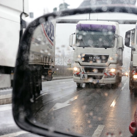 Lastwagen spiegeln sich auf regennasser Autobahn im Außenspiegel