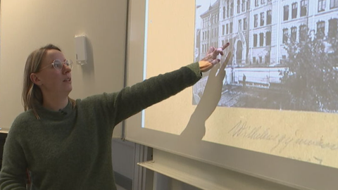 Lehrerin zeigt Schülern ein altes Bild ihrer Schule auf der Tafel