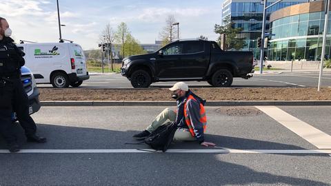 Ein Mann sitzt auf einer mehrspurigen Straße, vor ihm steht ein Polizist